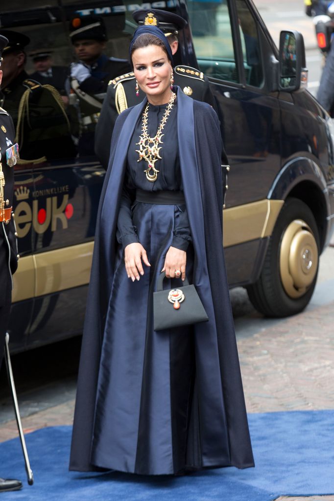 Mujer en elegante atuendo azul con capa, junto a oficiales militares.