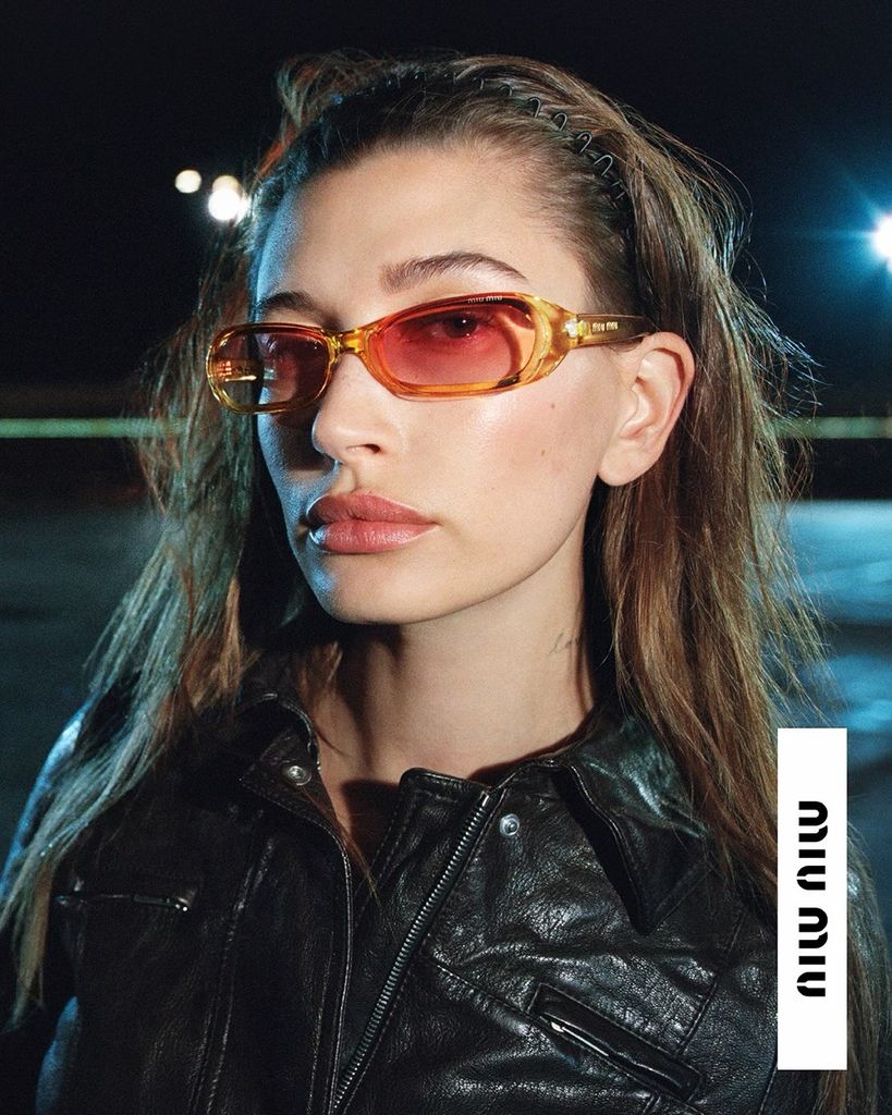 Hailey Bieber en una publicidad de Miu Miu con gafas ámbar, diadema zigzag y chaqueta de cuero