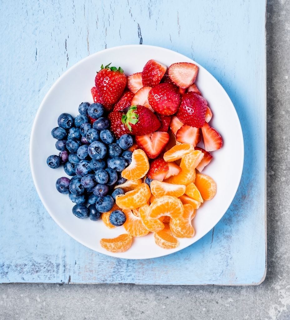Fresh fruit (strawberries, blueberries and tangerines) on a plate on blue background