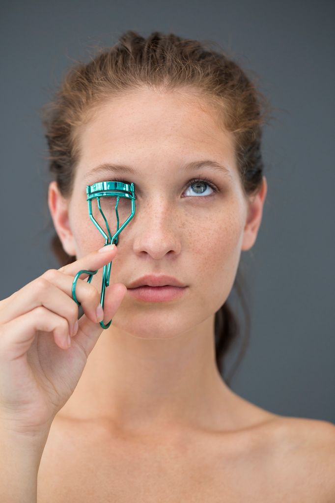Rostro de mujer mirando al techo mientras se riza las pestañas con un rizador azul aguamarina