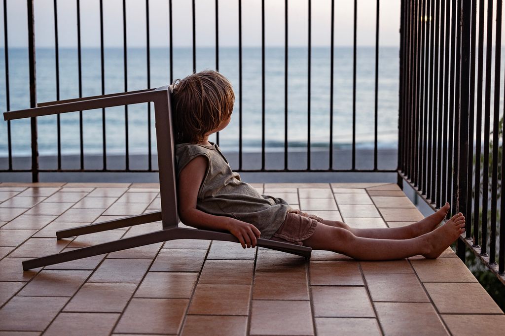 un niño está aburrido en la terraza, mirando al mar