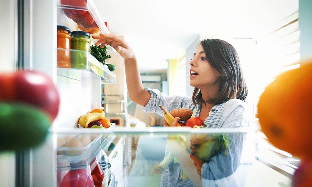 Mujer joven tomando vegetales y frutas de la nevera