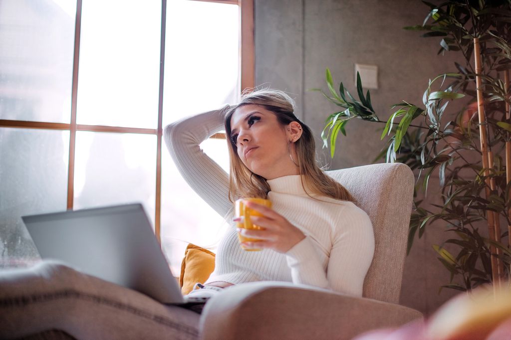 mujer joven, cansada, con una taza de café y su ordenador portátil en el sofá