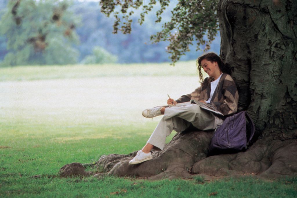 mujer leyendo y tomando notas bajo un árbol, en la naturaleza