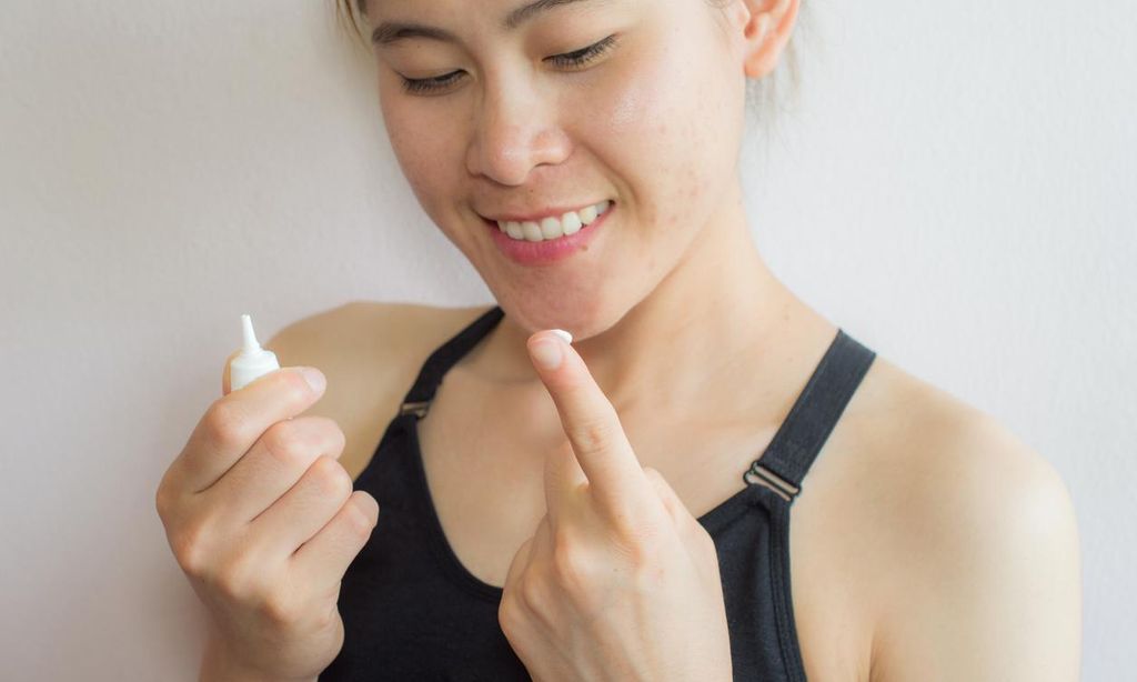 Mujer con acné observa producto de belleza