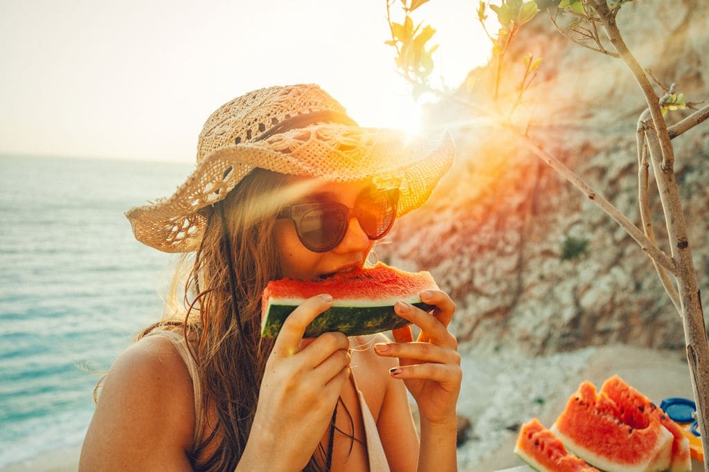 chica en la playa comiendo sandía