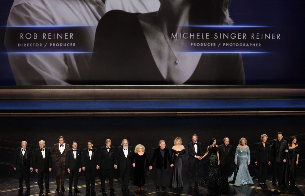 Michael McKean, Christopher Guest, Jerry O'Connell, Wil Wheaton, Fred Savage, Cary Elwes, Mandy Patinkin, Carol Kane, Billy Crystal, Meg Ryan, Kiefer Sutherland, Demi Moore, Kevin Pollak, Kathy Bates, Annette Bening, John Cusack and Daphne Zuniga stand onstage in front of a screen showing a photo of late US director Rob Reiner and his wife late US photographer Michele Reiner during the 98th Annual Academy Awards at the Dolby Theatre in Hollywood, California on March 15, 2026. (Photo by Patrick T. Fallon / AFP via Getty Images)