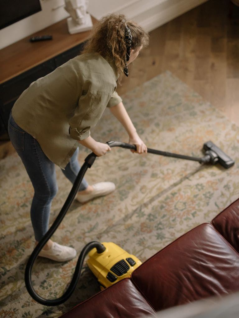 Mujer limpiando con una alfombra con el aspirador.