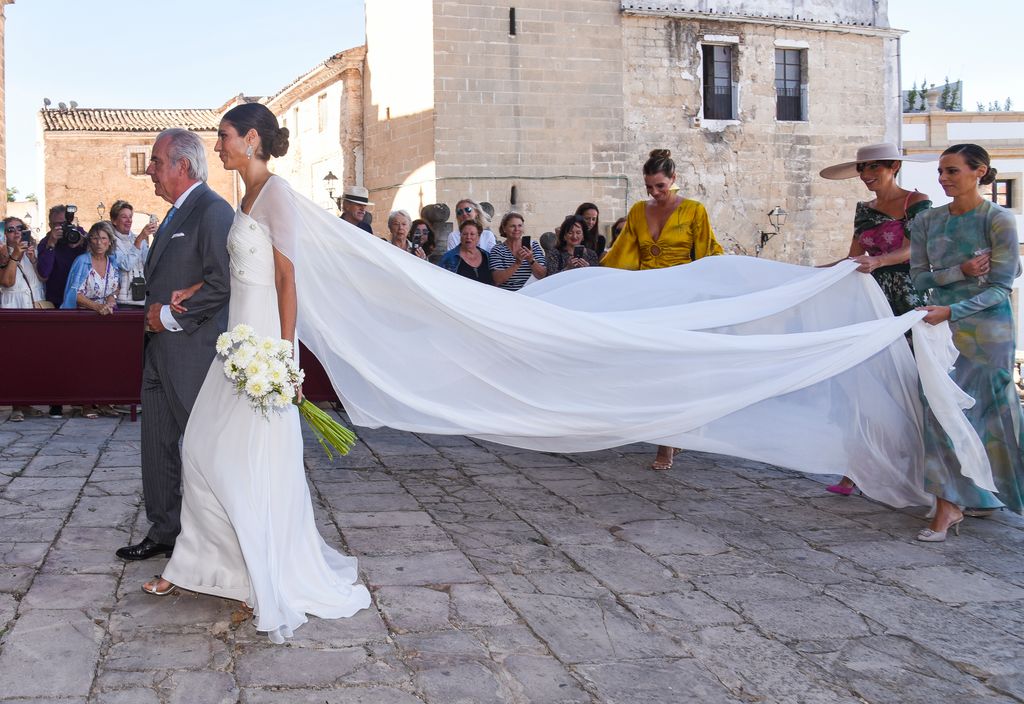 La novia llegando a la iglesia del brazo de su padre y seguida por sus tres hermanas