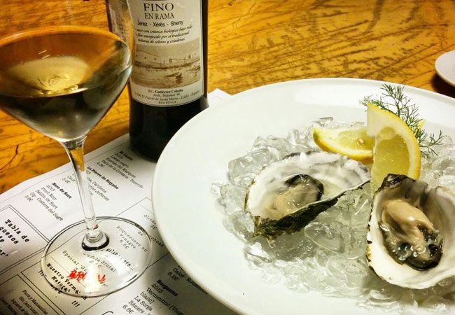 Botella de vino Fino en Rama, ostras en hielo y limón en plato blanco.