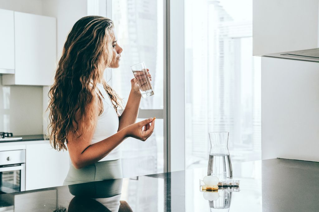 mujer joven tomando suplementos en la cocina