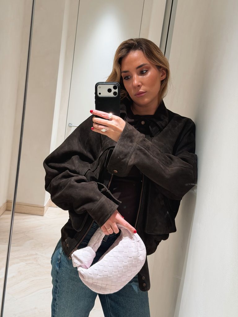 Alice Campello con vaqueros, cazadora de ante marrón y bolso blanco haciéndose un selfie