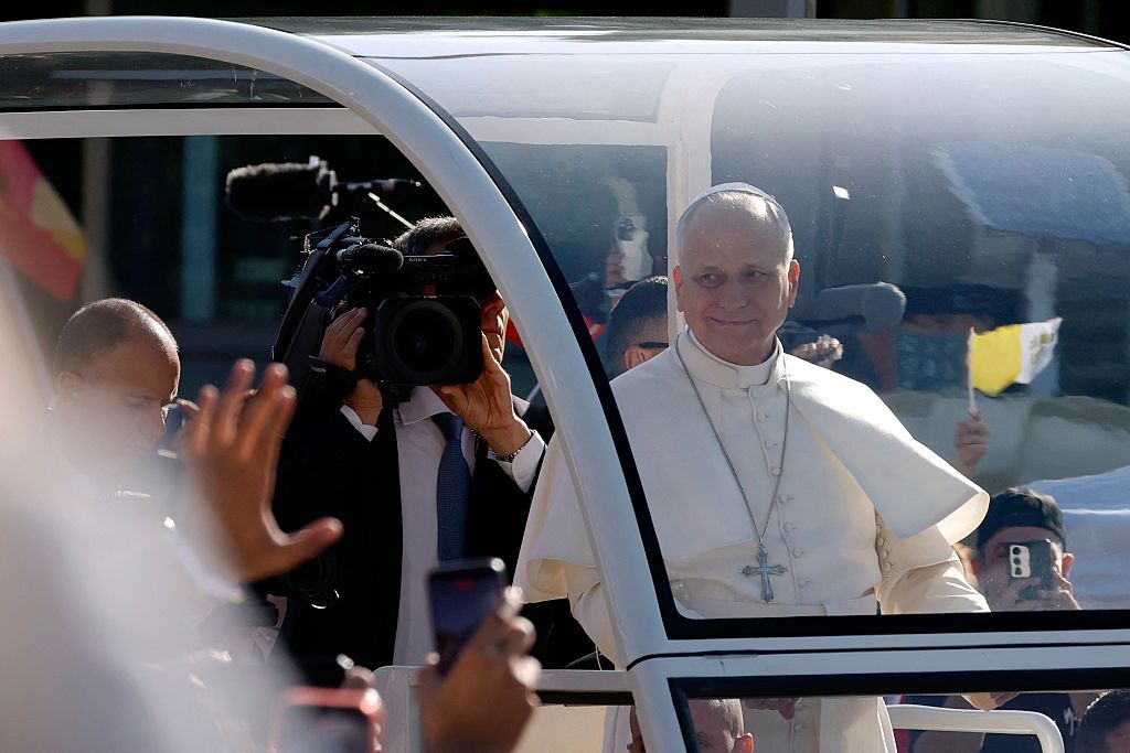 Papa Francisco sonríe desde un vehículo papal, rodeado de cámaras y fieles.