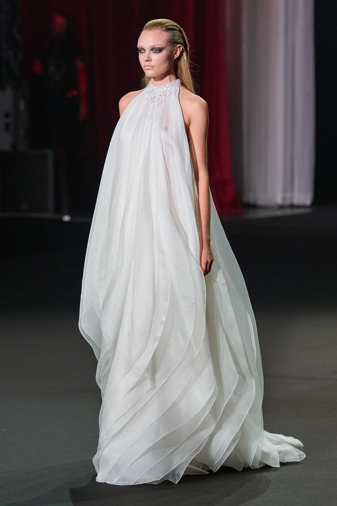 Sasha Pivovarova camina en una pasarela con un vestido blanco largo y fluido.