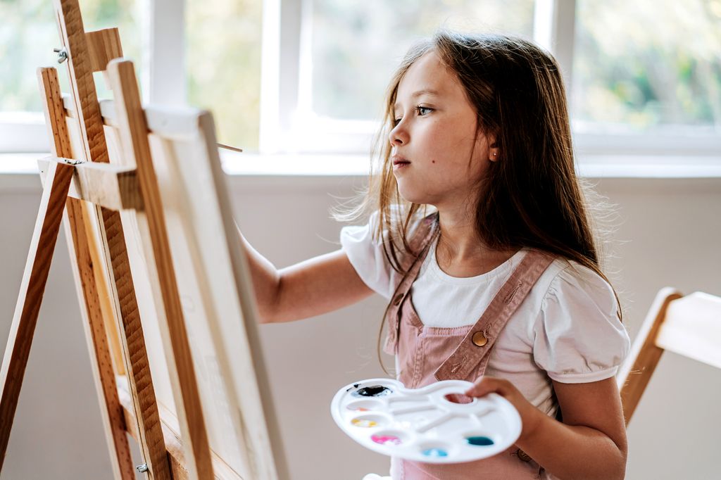 niña feliz pintando un cuadro en un caballete