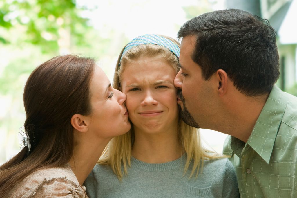 Adolescente haciendo una mueca mientras sus padres le dan un beso