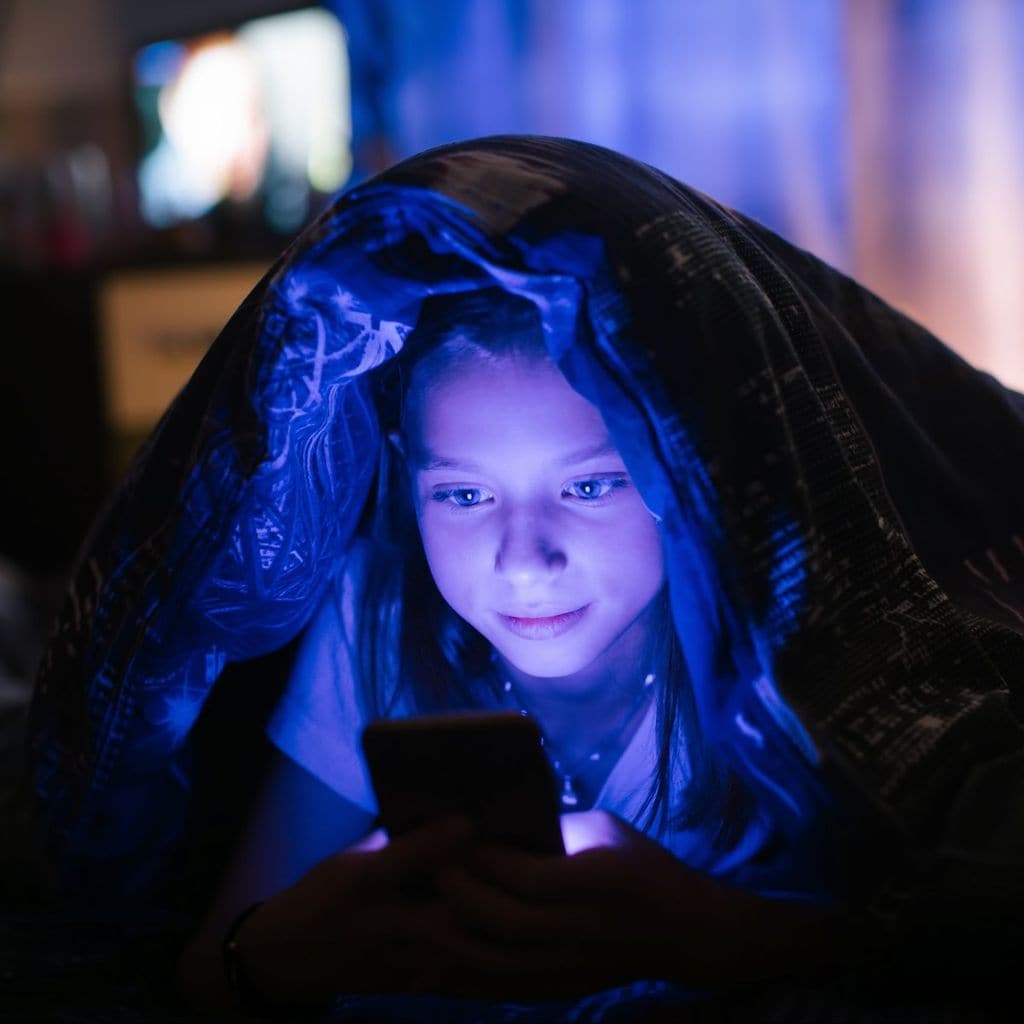 Niña con teléfono móvil en la cama por la noche