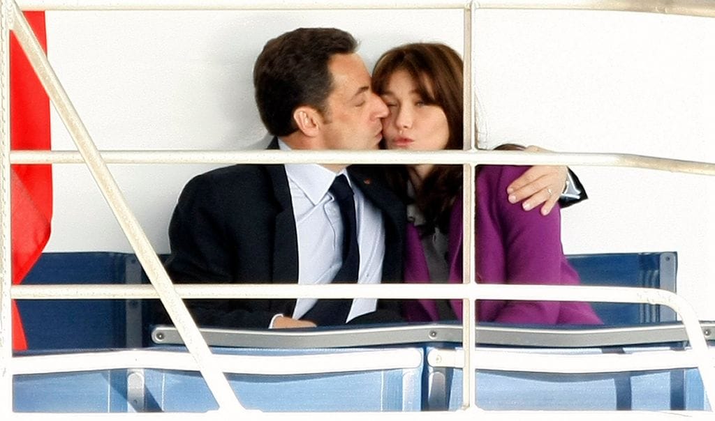 Plano medio de Nicolas Sarkozy dando un beso a Carla Bruni en un viaje