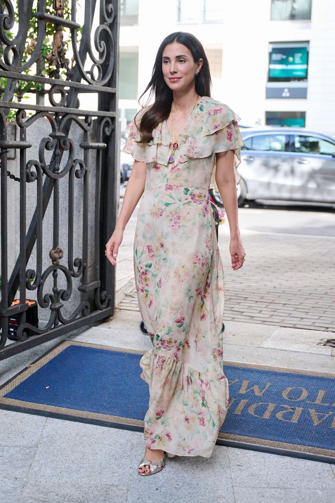 Mujer con pelo largo y vestido floral caminando en la entrada de un edificio.