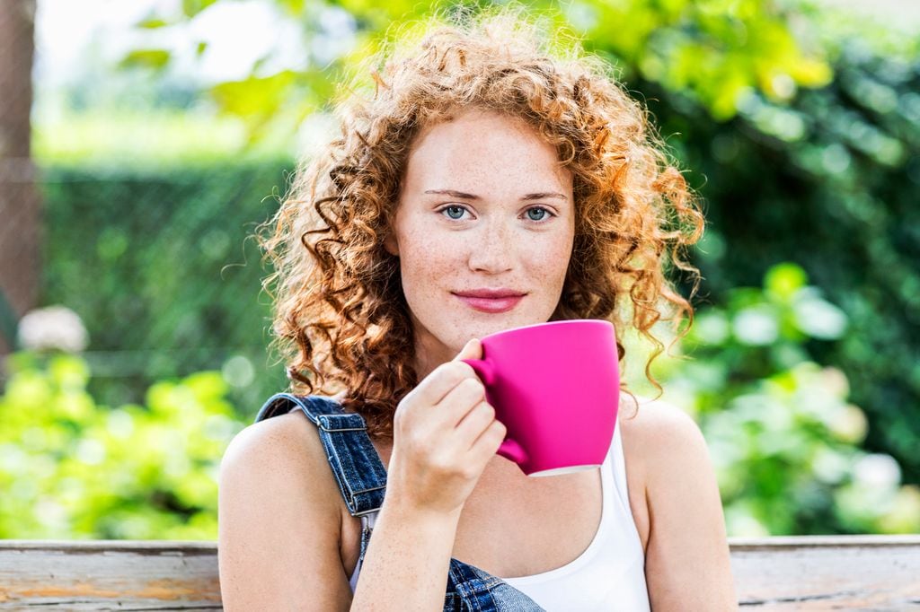 Mujer pelirroja y con el pelo rizado tomándose una infusión en una taza rosa