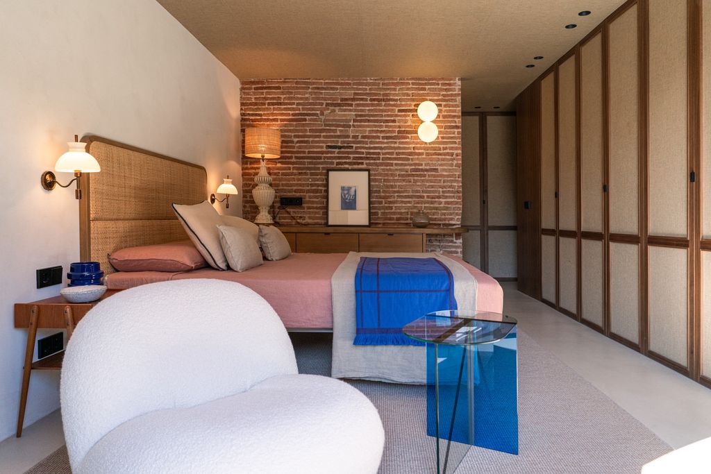 Dormitorio con pared de ladrillo y cuadro apoyado sobre un mueble. 