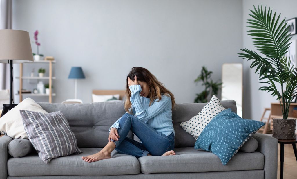 Mujer deprimida en el sofá tapándose la cara con la mano
