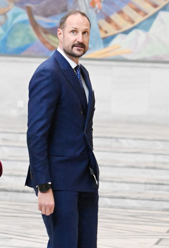 Plano medio de Haakon de Noruega con traje azul marino atendiendo una visita