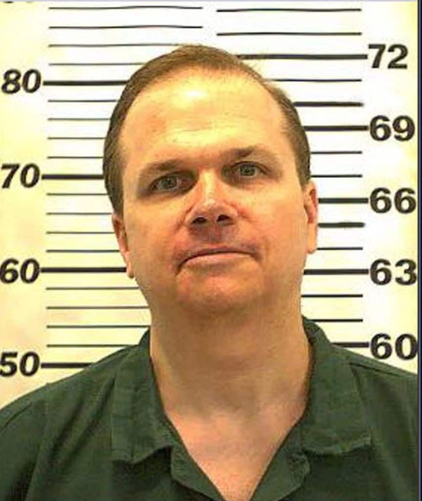 Hombre en camisa verde frente a una tabla de medidas, expresión seria.