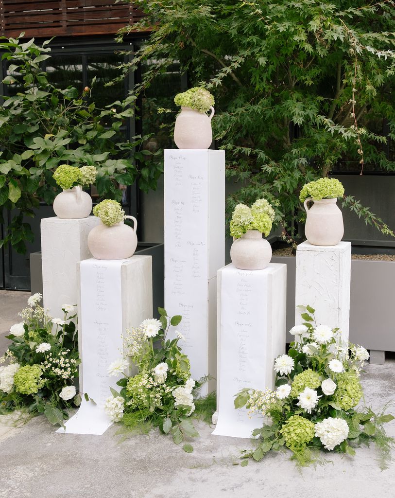 Seating plans de boda en columnas vasijas y flores verdes