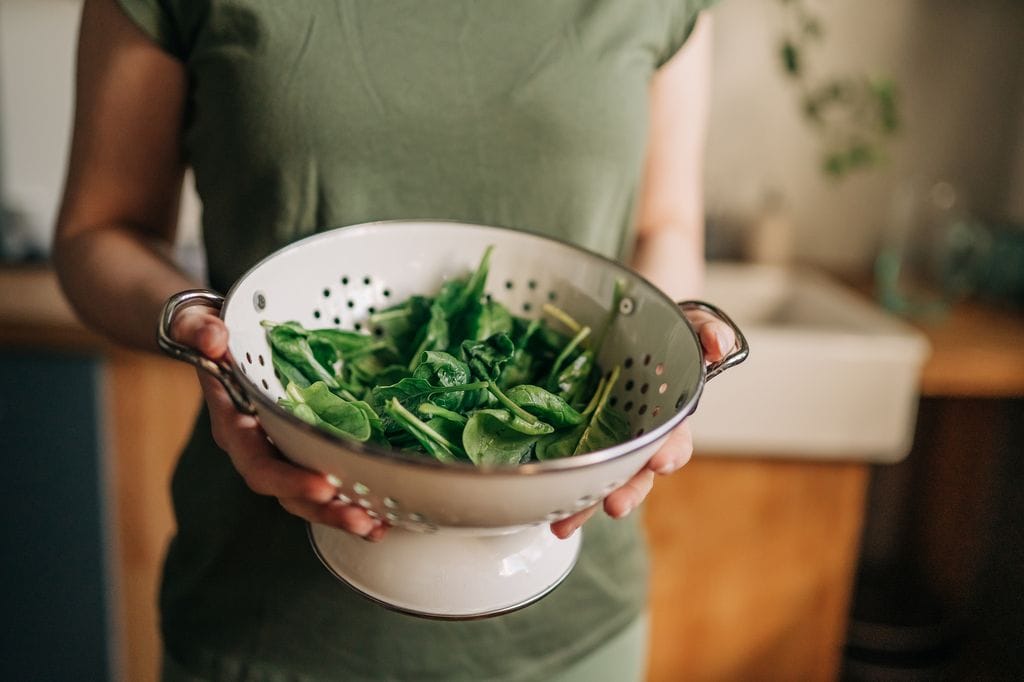 mujer con un bol con espinacas y otras verduras de hoja verde