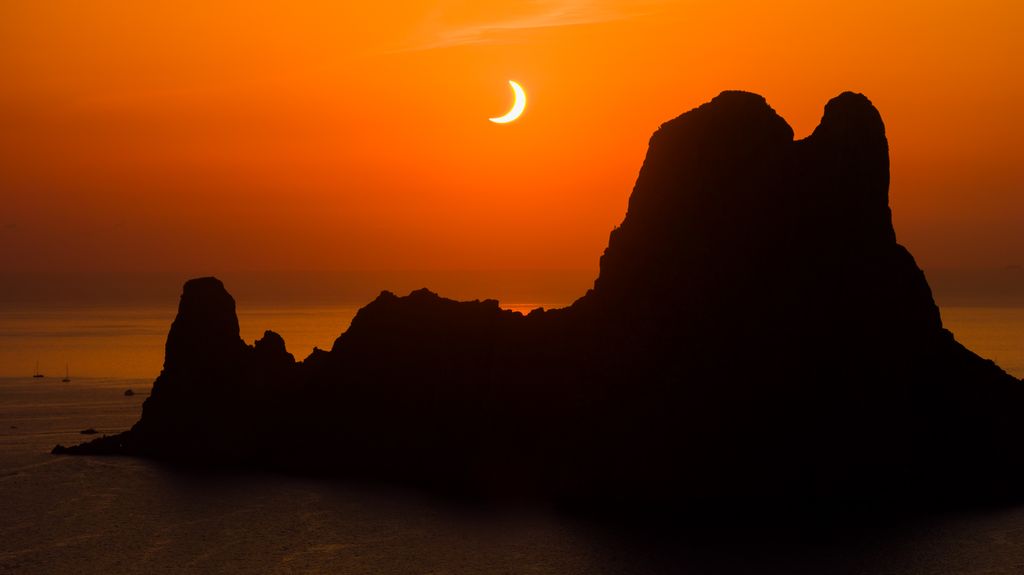 El Sol, reducido a un fino creciente luminoso, se recorta sobre la costa de Ibiza, teñida por intensos tonos anaranjados.