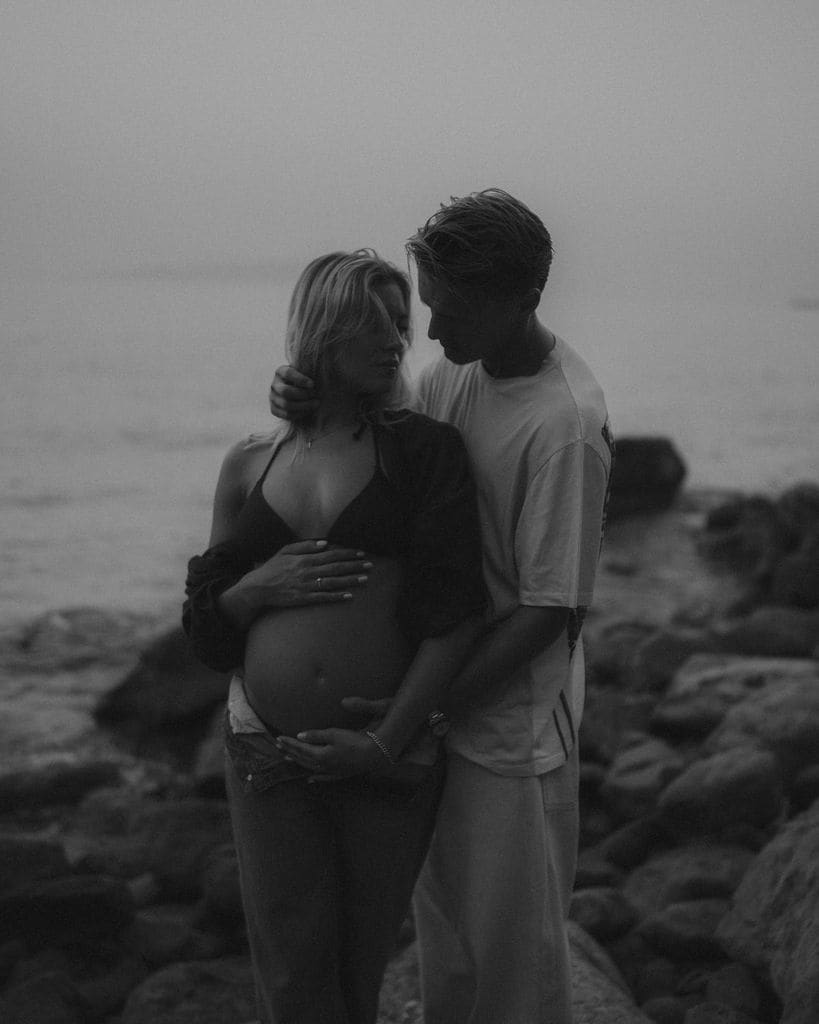 Plano medio de Helene Spilling y Martin Odegaard posando esperando un hijo en una playa