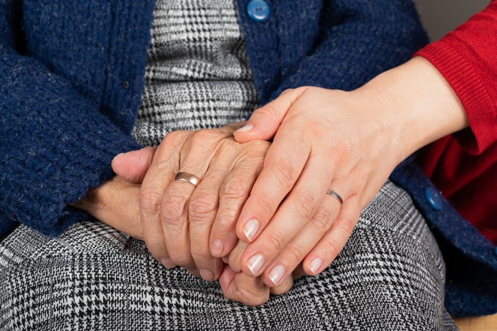 Manos jóvenes abrazan unas manos mayores