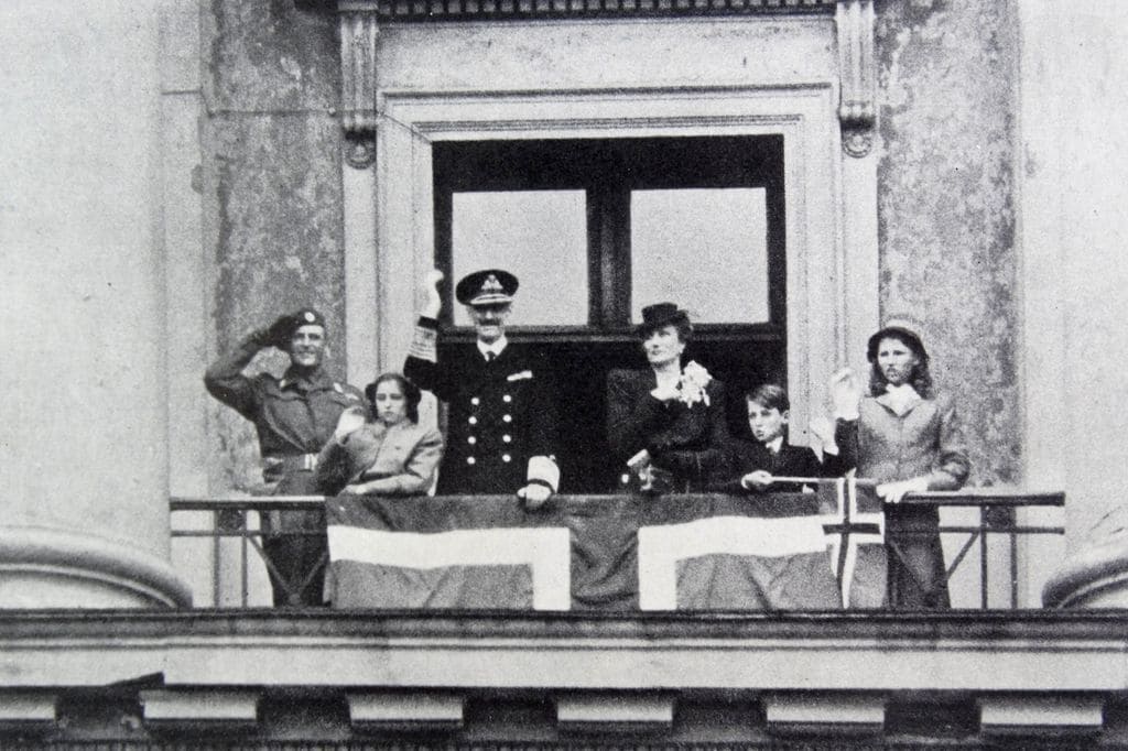 Esta es una fotografía histórica y aunque no corresponde exactamente con la festividad nacional se vivió como si lo fuera, ya que la Familia Real regresaba en junio de 1945 del exilio tras la Segunda Guerra Mundial y cuando Noruega fue ocupada por la Alemania nazi. Entonces el rey, en el centro de la imagen, era Haakon VII, el primero de su dinastía y abuelo del rey Harald. A la izquierda de la imagen está el príncipe heredero, Olav, y el niño pequeño es su hijo, el actual rey Harald. También está la princesa Marta de Suecia, que era la mujer de Olav, y falleció antes de llegar a reinar, las dos niñas son las hermanas mayores del rey Harald, la polémica y fallecida princesa Ragnhild, a la derecha de la imagen, y entre su padre y su abuelo, está la princesa Astrid, que sigue siendo un miembro activo de la Familia Real noruega. 