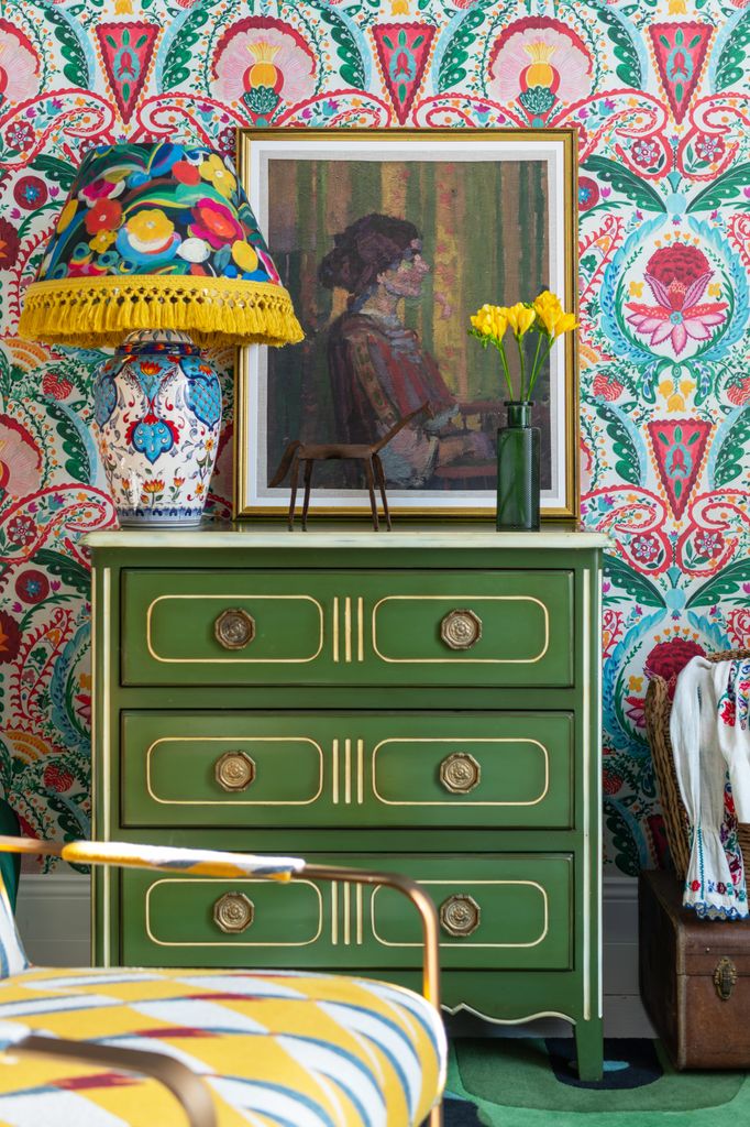 Cómoda de madera pintada en verde apoyada en pared con papel pintado