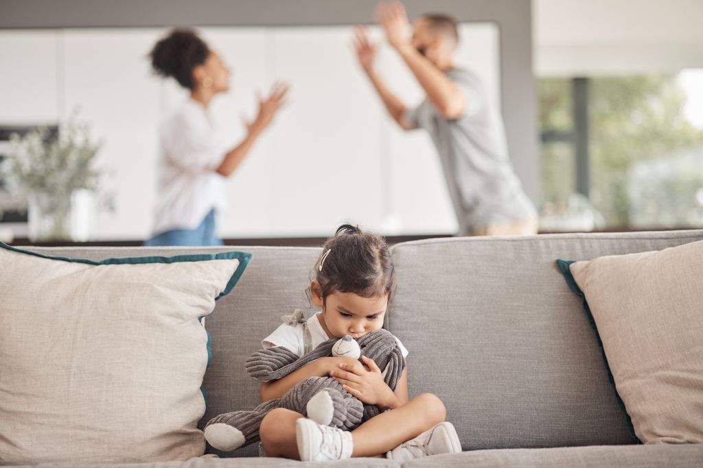 Niña pequeña agarrada a un peluche con sus padres detrás discutiendo