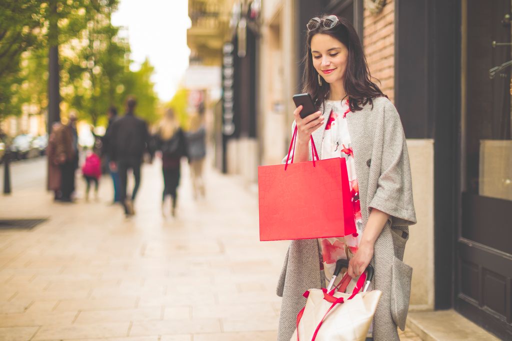 Mujer con bolsas de compras en la calle mirando su teléfono móvil