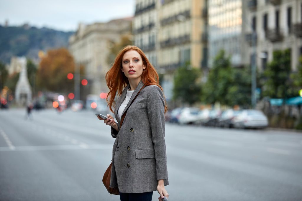 mujer pelirroja caminando por la calle con el móvil en la mano