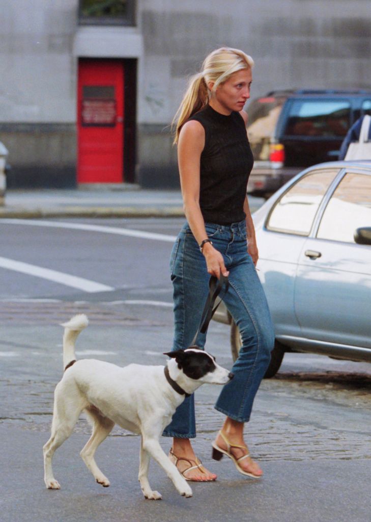 Carolyn Bassette con pantalones vaqueros boot cut, top negro y sandalias sacando a su perro en Nueva York
