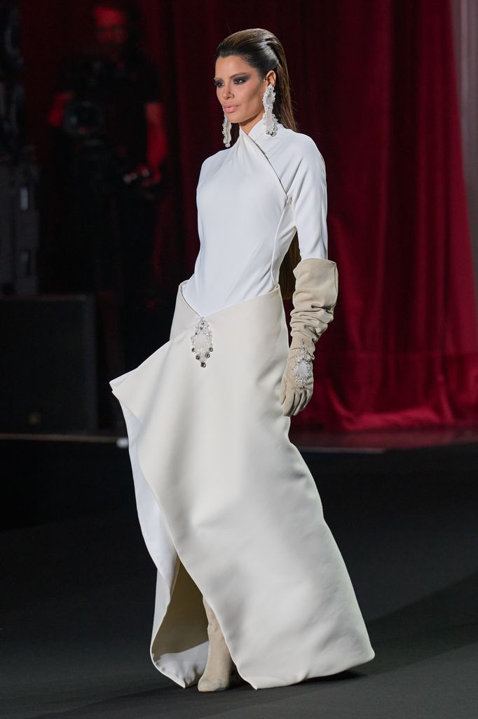 Ariadna Gutiérrez camina en una pasarela con un vestido blanco y guantes.