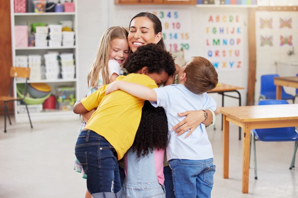 Alumnos en clase abrazando a la profesora