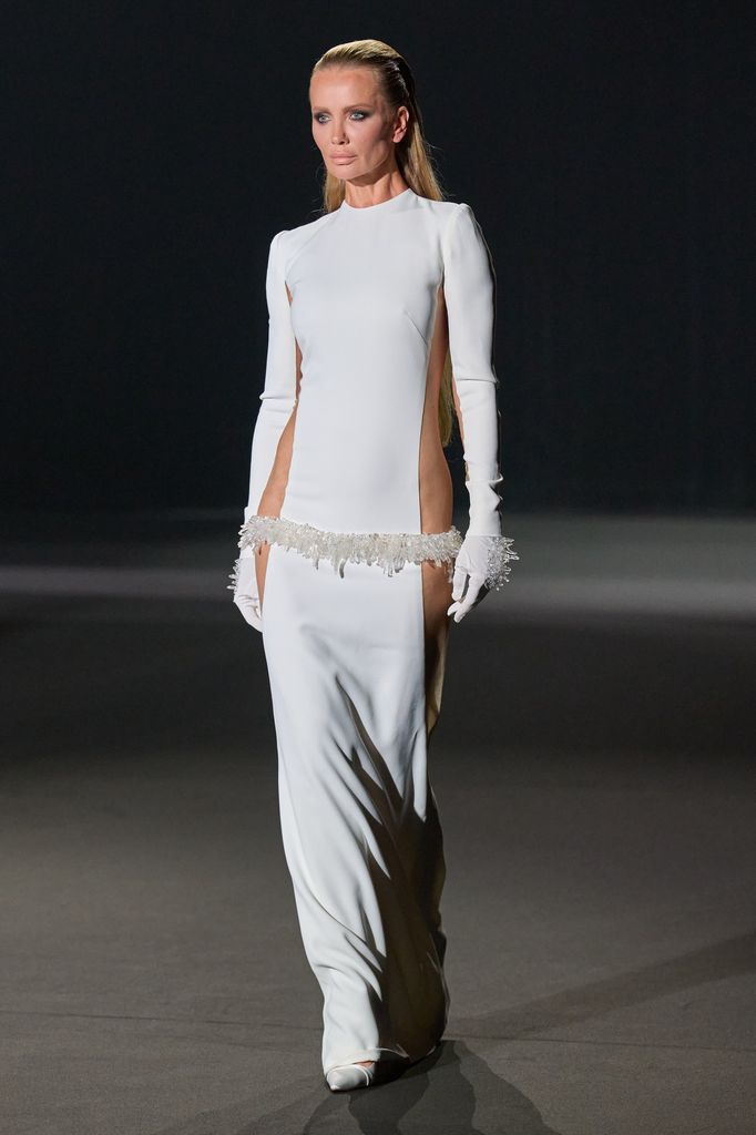 Modelo caminando en pasarela con vestido blanco y guantes largos.