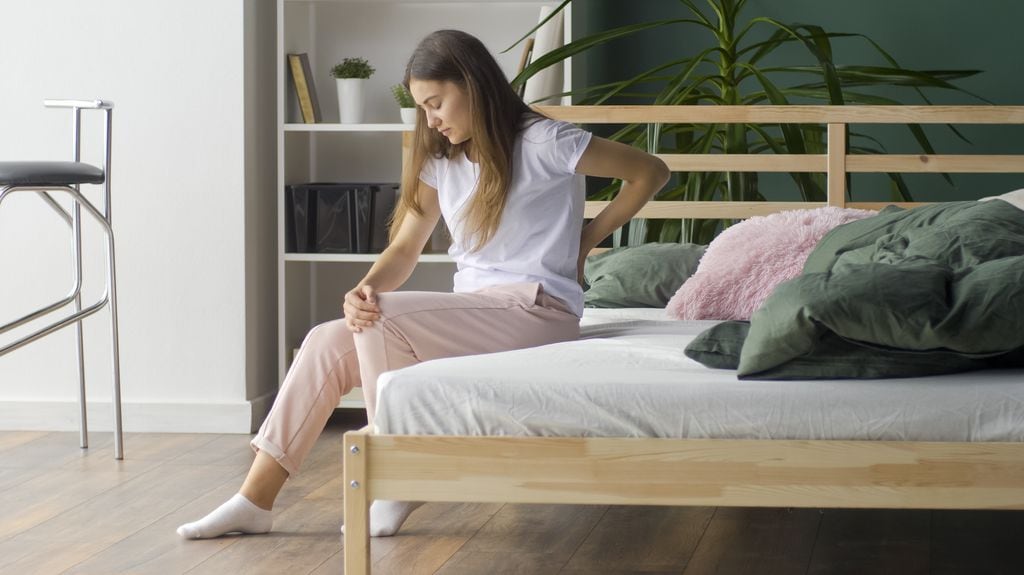 mujer joven con dolor de espalda sentada en la cama