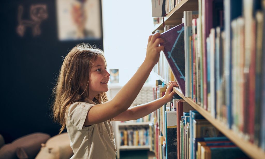 ni a eligiendo en un libro en una estanteria de una biblioteca
