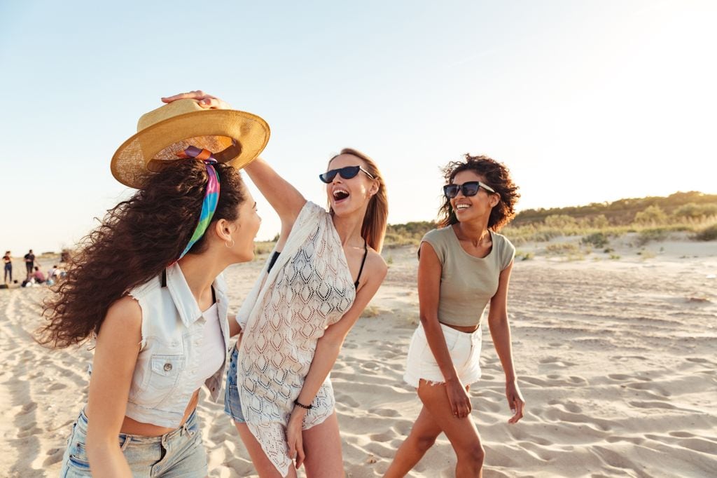 tres amigas felices y sonrientes en la arena de la playa