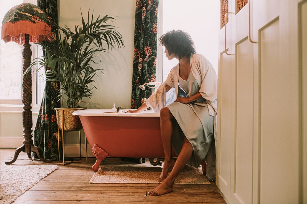 mujer sentada en la bañera, preparando un baño relajante