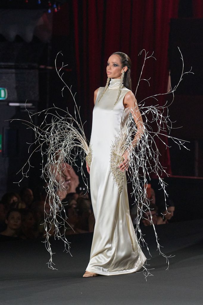Modelo en pasarela con vestido blanco y accesorios de ramas plateadas.