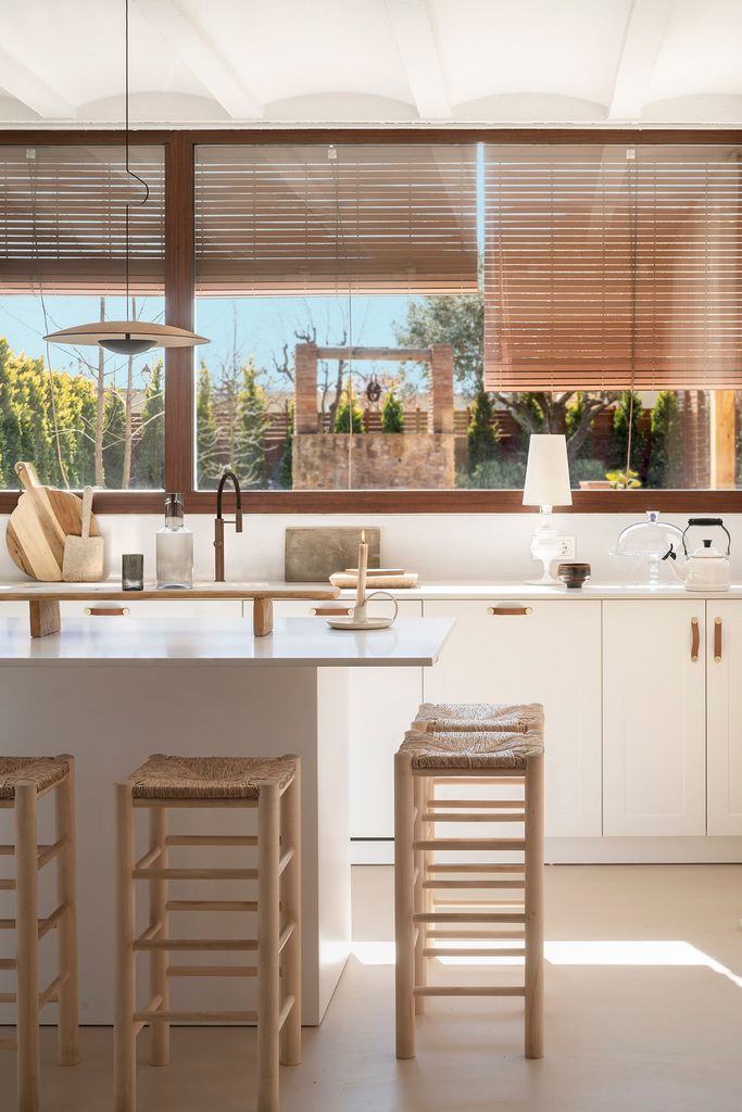 Cocina blanca con una isla central que se acompaña con taburetes de factura artesanal