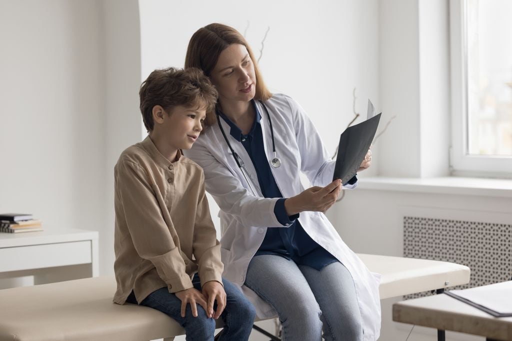 Niño con osteoporosis viendo con la médico una radiografía