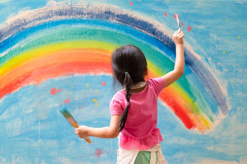 Niña pintando un arcoíris en la pared